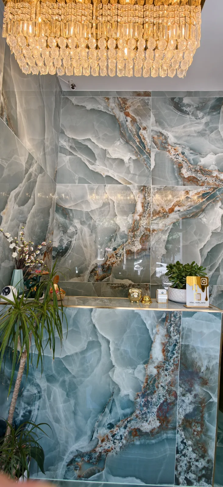 Recepción de Bilbao Beauty Center con mostrador, pared de tonos turquesa y lámpara dorada